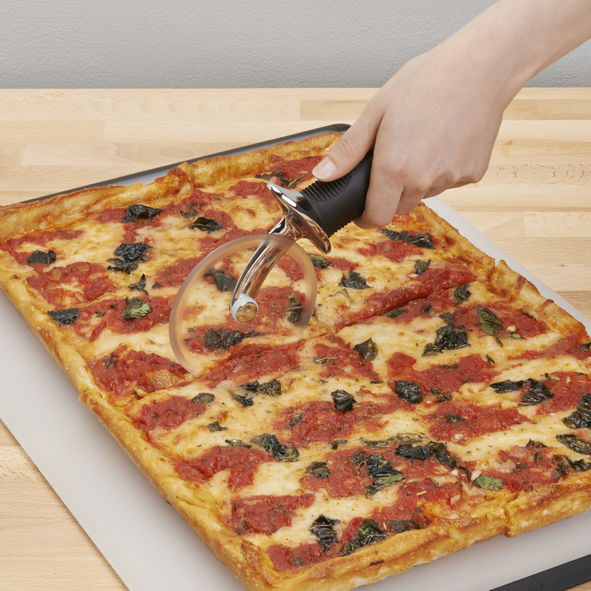 hand using pizza wheel to cut square pizza on cutting board.