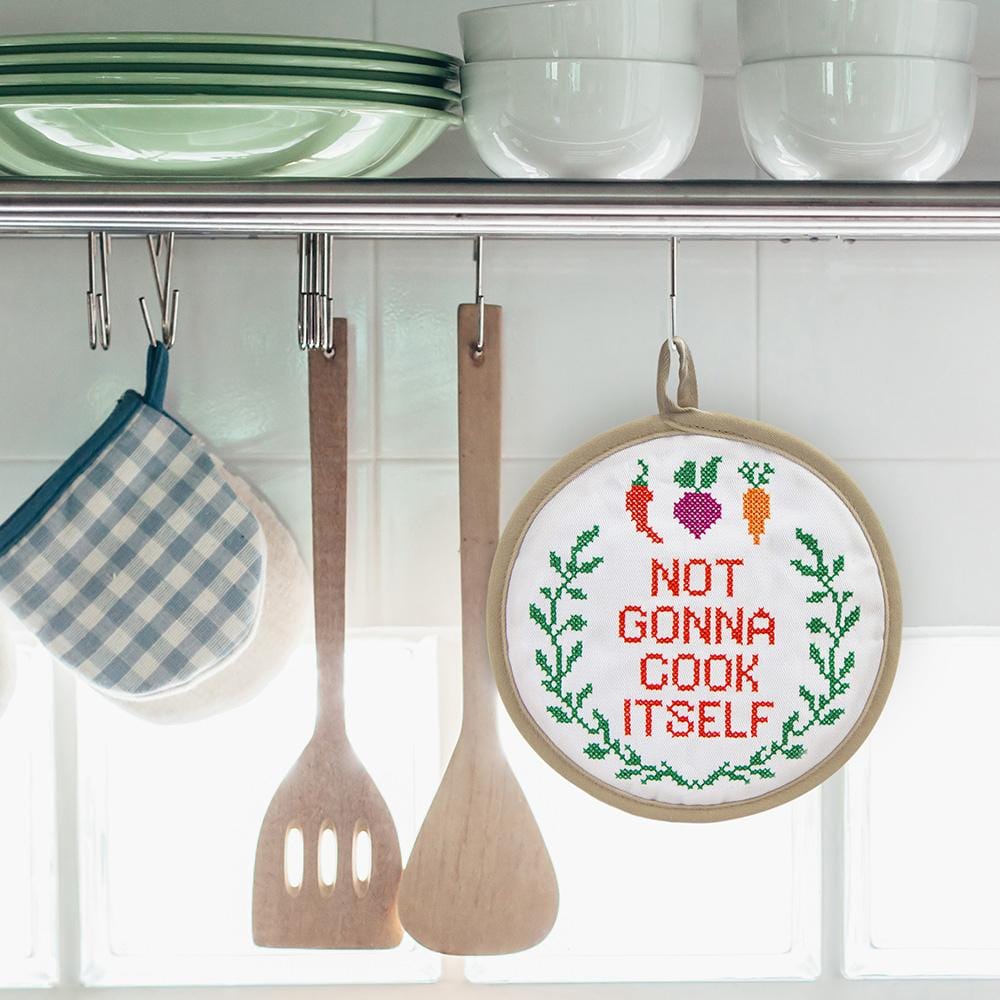 "not gonna cook itself" potholder hanging in a kitchen next to wooden utensil and oven mitt