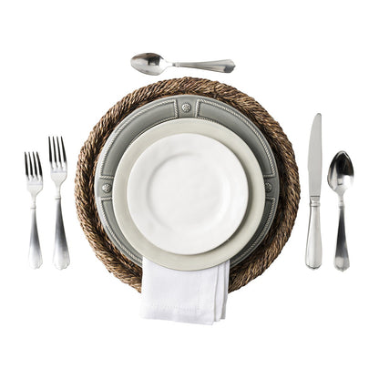 place setting of puro dishes on a seagrass charger next to flatware on a white background