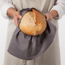 person holding loaf of bread wrapped in flour sack towel.