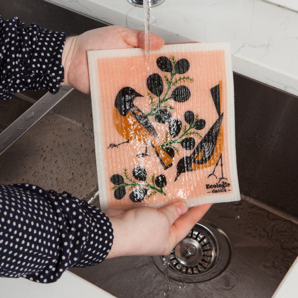 hands holding swedish dish cloth under sink faucet.