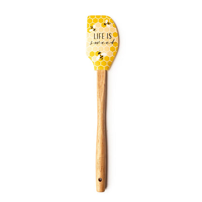 yellow spatula with honey comb, bees, and "life is sweet" printed on it and a wooden handle.