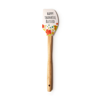 white spatula with "happy thankful blessed" and a floral design printed on it and a wooden handle.