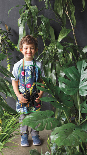 kid wearing apron surrounded by house plants.