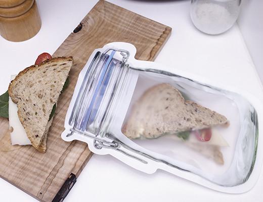 large mason jar zipper bag displayed with a sandwich grinder a wood plank on a white background
