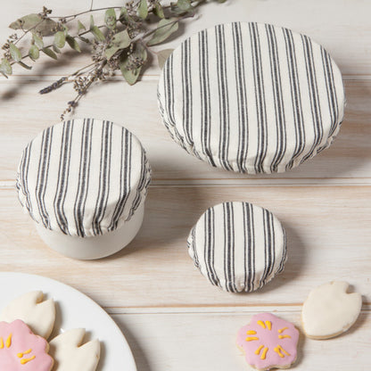 all three sizes of ticking mini bowl covers on white bowls displayed on a whitewashed wood slat surface next to a plate of cookies