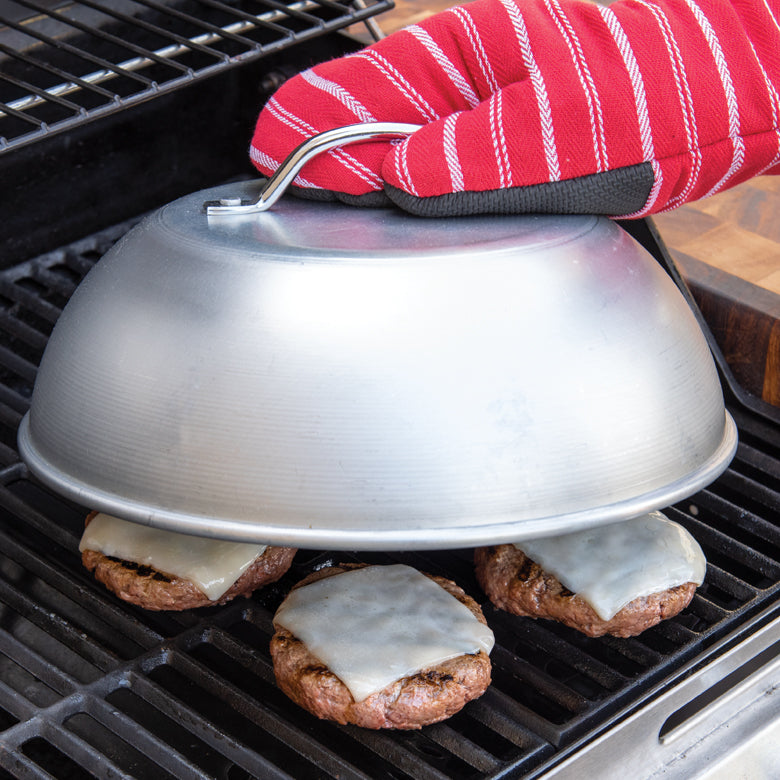 hand holding handle of domed lid over grill with burgers on it.