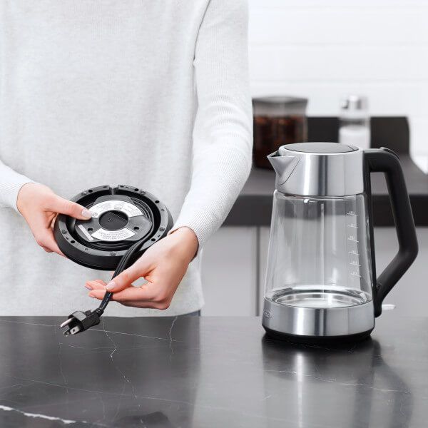 hand holding base of kettle showing where the cord winds into it; kettle sitting next to person.