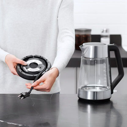 hand holding base of kettle showing where the cord winds into it; kettle sitting next to person.