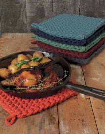 cast iron skillet set on a clay knit pot holder and a stack of assorted knit pot holders behind it.