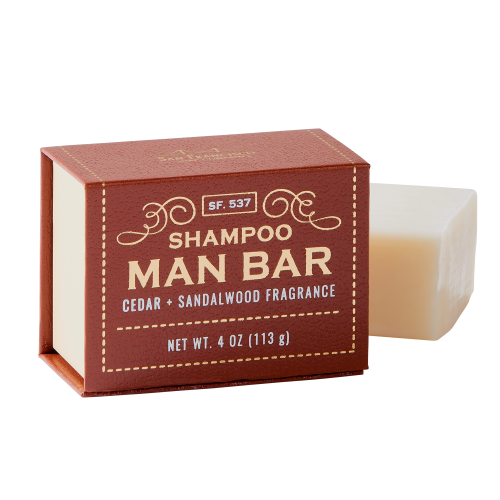 brown rectangular box of soap with bar of soap behind it on white background. box has "man bar" written in gold, swirling gold graphics above text, and gold dotted line bordering the box edges.