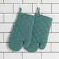 two lagoon heirloom stonewash oven mitts hanging against a white tile background