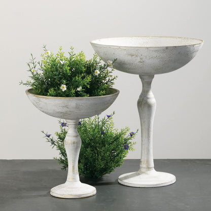 both sizes of rustic pedestal bowls with a green bunch in the small one and next to it on a dark gray surface