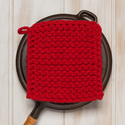 red knit potholder  set on a black cast iron skillet on a wooden table.