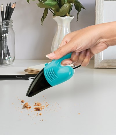 hand holding mini vacuum over crumbs on a desk.