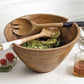 wooden serving bowl filled with salad and displayed with serving utensils oil bottles, plates, and stripped napkins