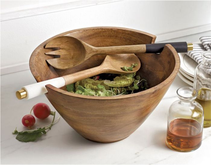 wooden serving bowl filled with salad and displayed with serving utensils oil bottles, plates, and stripped napkins