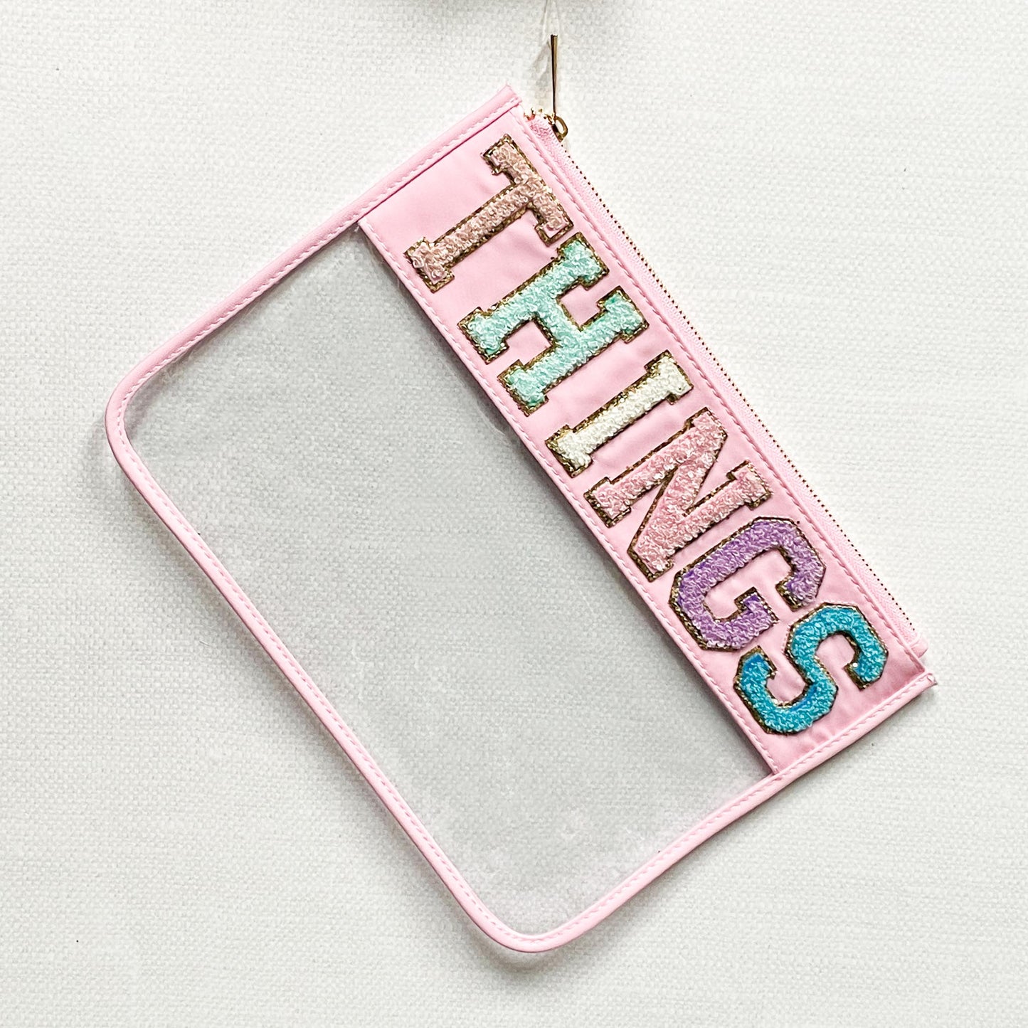 clear nylon bag with pink trim and chenille patches that spell "things".