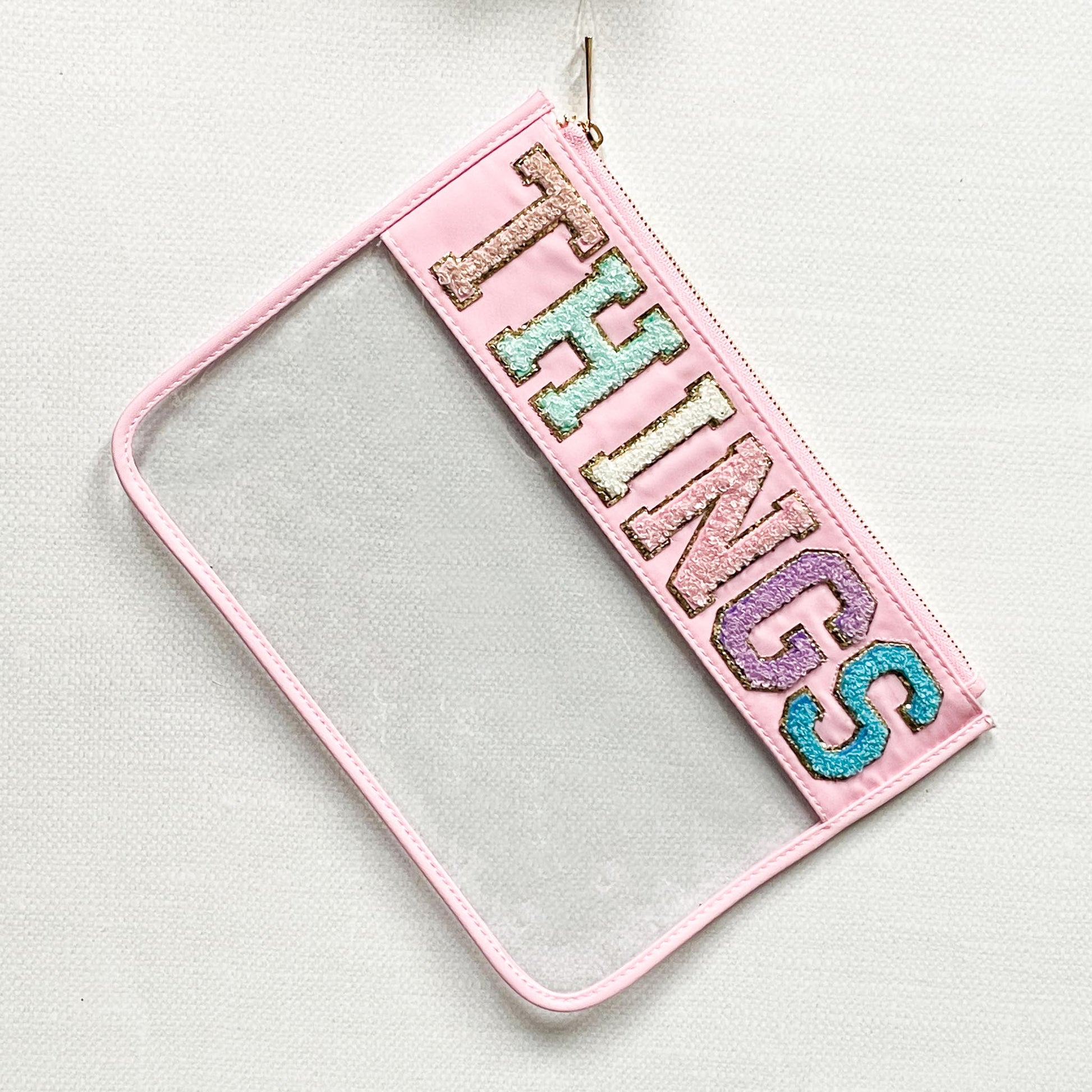 clear nylon bag with pink trim and chenille patches that spell "things".