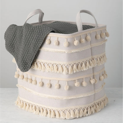 pom pom basket displayed with a gray blanket hanging over the side on a white surface