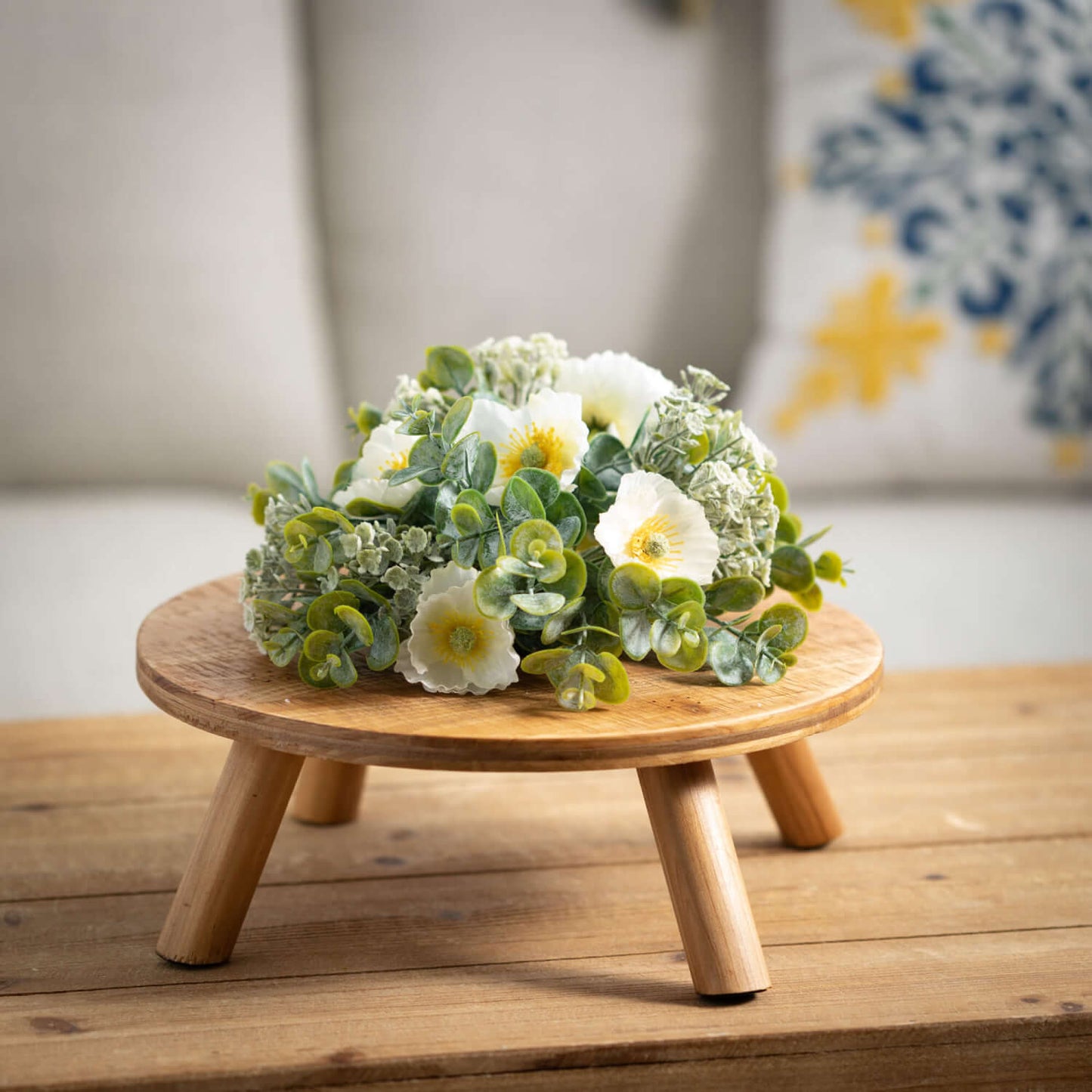 riser on wooden table with floral arrangement on it. couch and pillow in background.