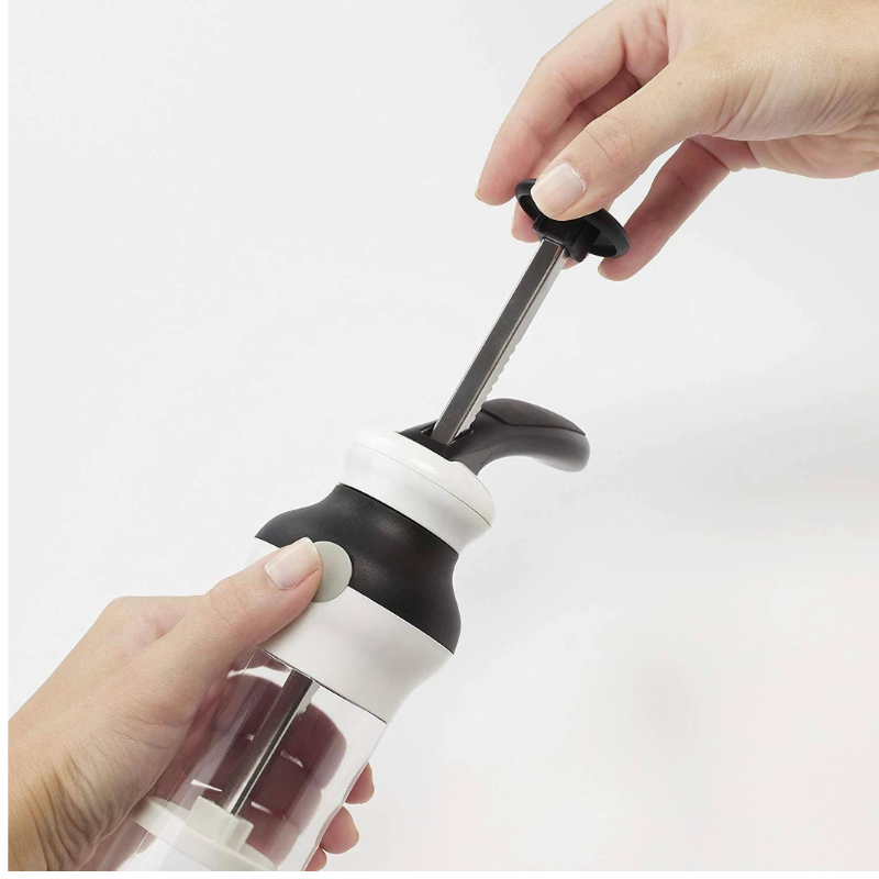 two hands hold the Oxo cookie press to demonstrate the push down lever on a white background.