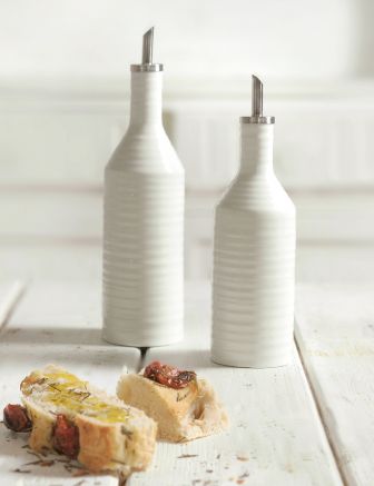small and large oil bottles on a white wooden table with slices of bread topped with oil and herbs.