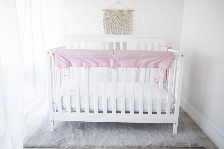 pink crib chomper displayed on a white crib in a child's room