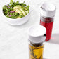 top view of dispenser bottles filled with oil and vinegar on countertop with bowl of salad in background.