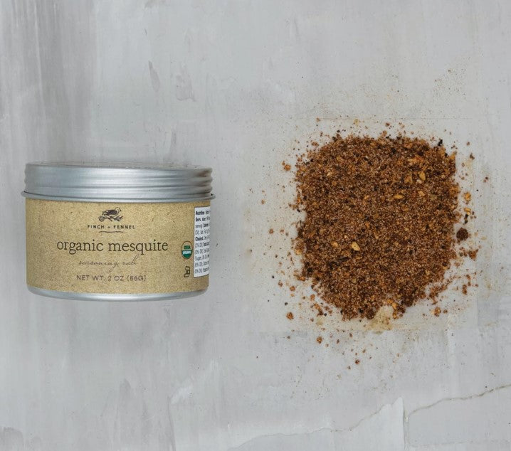 a tin of organic mesquite seasoning displayed next to a small mound of scattered seasoning on a white background