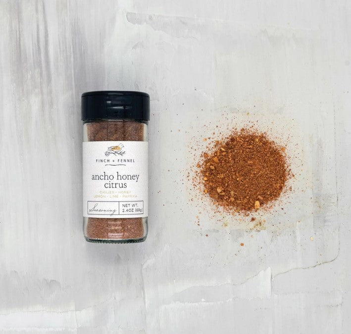 jar of ancho honey citrus seasoning laying down next to a scatter pile of seasoning on a white surface