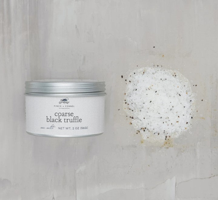 a tin of course black truffle salt displayed next to a small mound of scattered seasoning on a white background