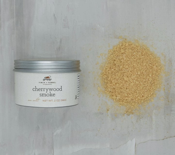 a tin of cherrywood smoked sea salt displayed next to a small mound of scattered seasoning on a white background