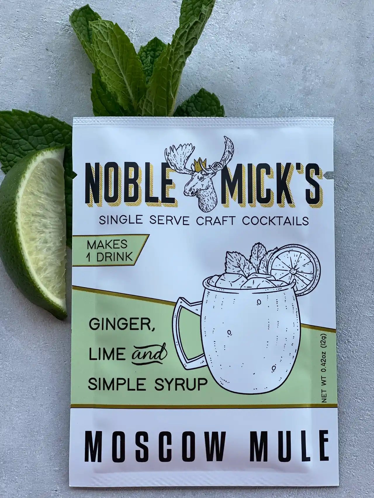 noble mick's single serve packet of Moscow Mule mix on a bar top with mint and a lime.