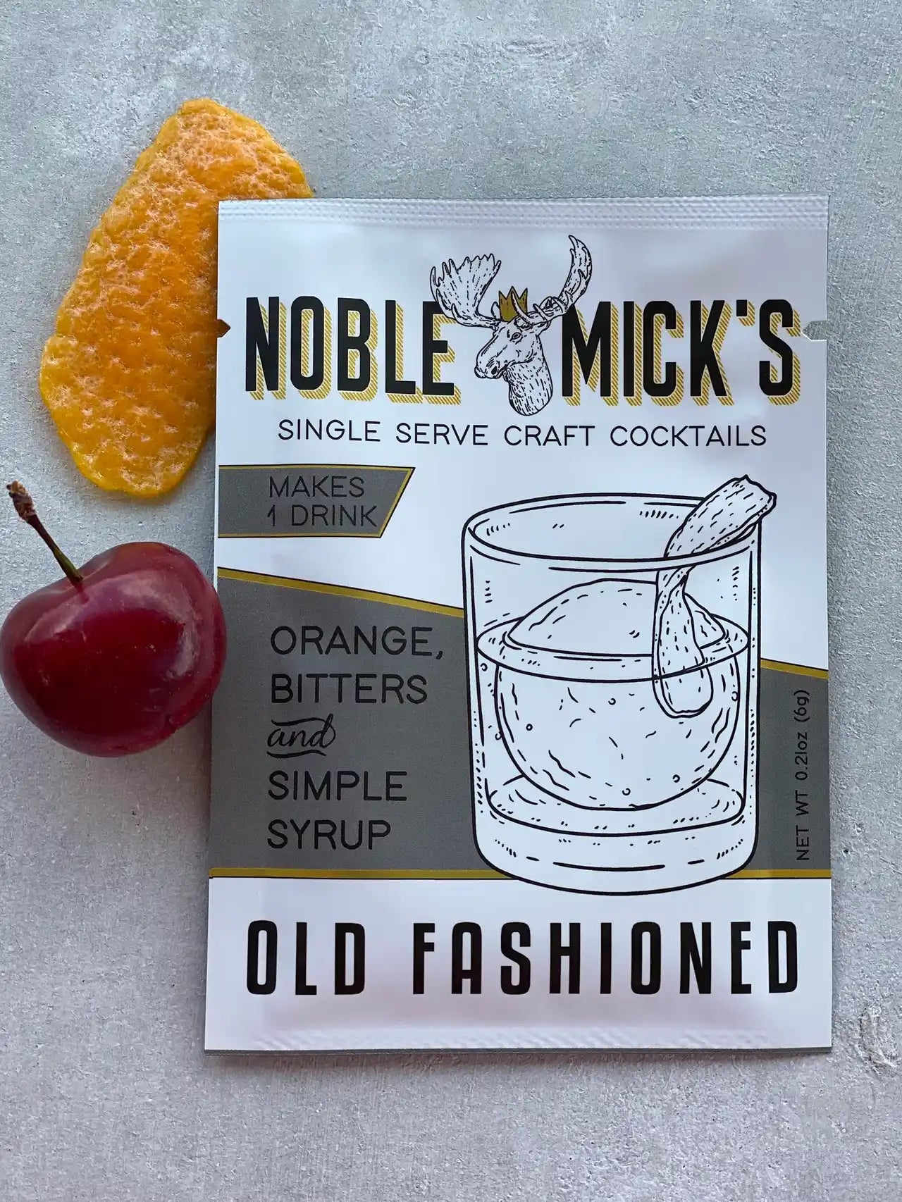 noble mick's single serve packet of Old Fashioned mix on a bar top with a cherry and an orange peel.