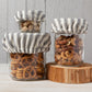 three different size jars filled with pretzels and nuts with the ticking mini bowl covers on and displayed on a tree cookie cut