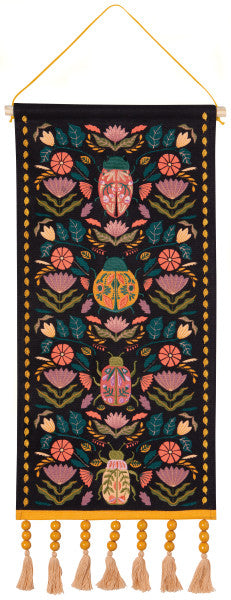 black amulet wall art with flowers, scarabs, and beetles in pinks and green hues with yellow beaded tassels