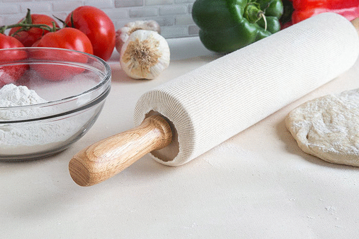 view of end of rolling pin with cover on it on counter with dough and bowl of flour.