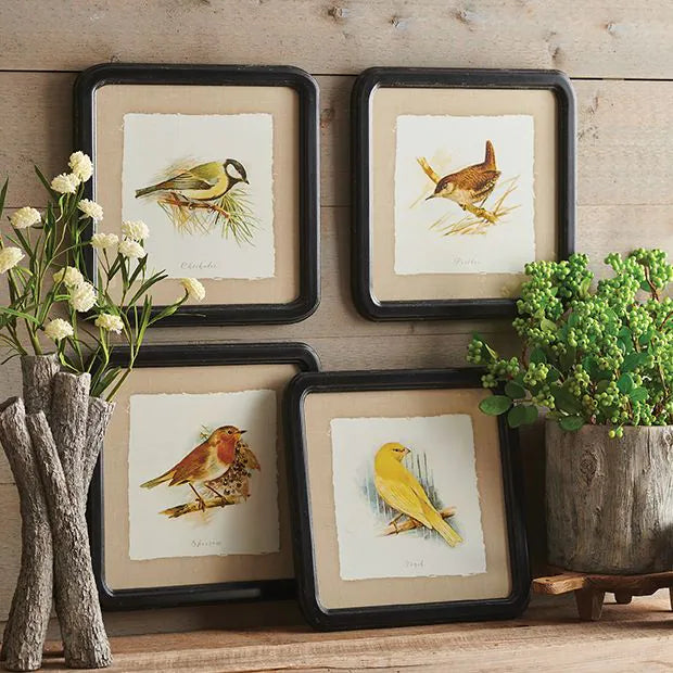 4 bird prints above a wooden table with vases and greenery.