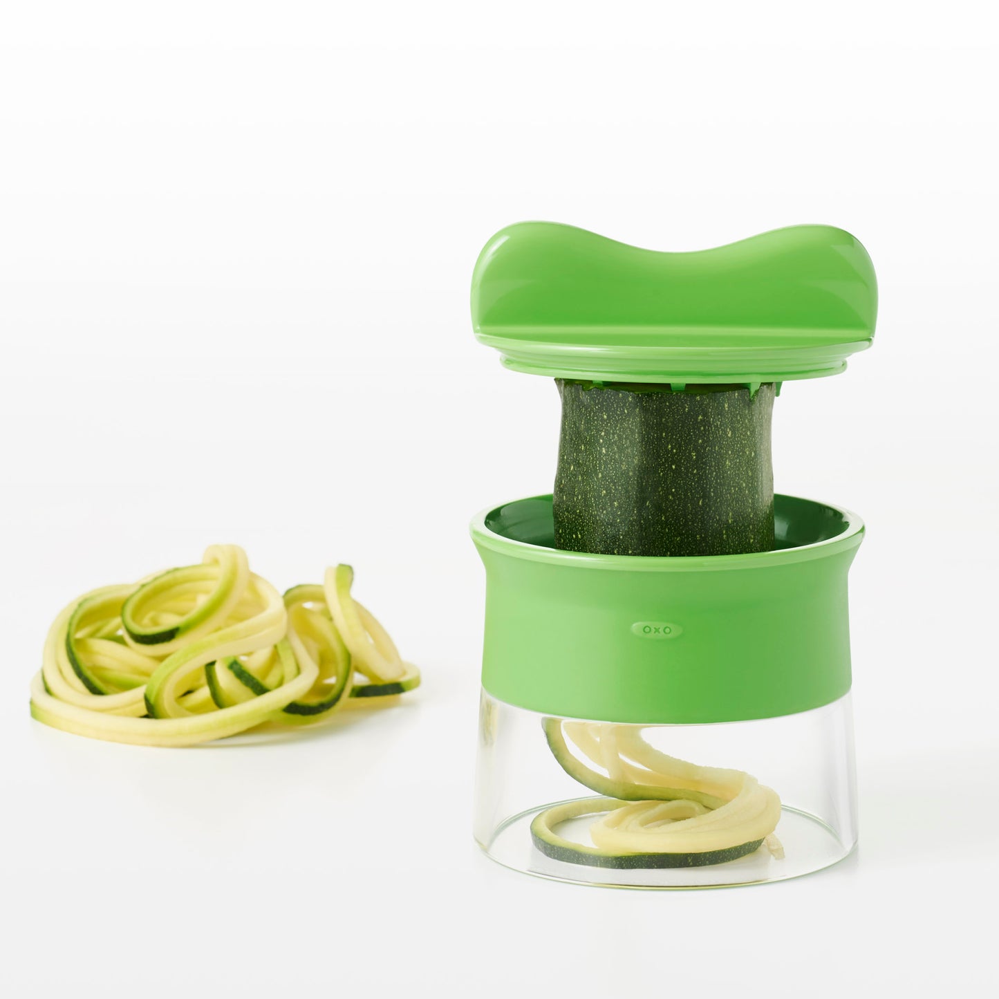 spiralizer with zucchini in it and pile of spiralized zucchini in background.