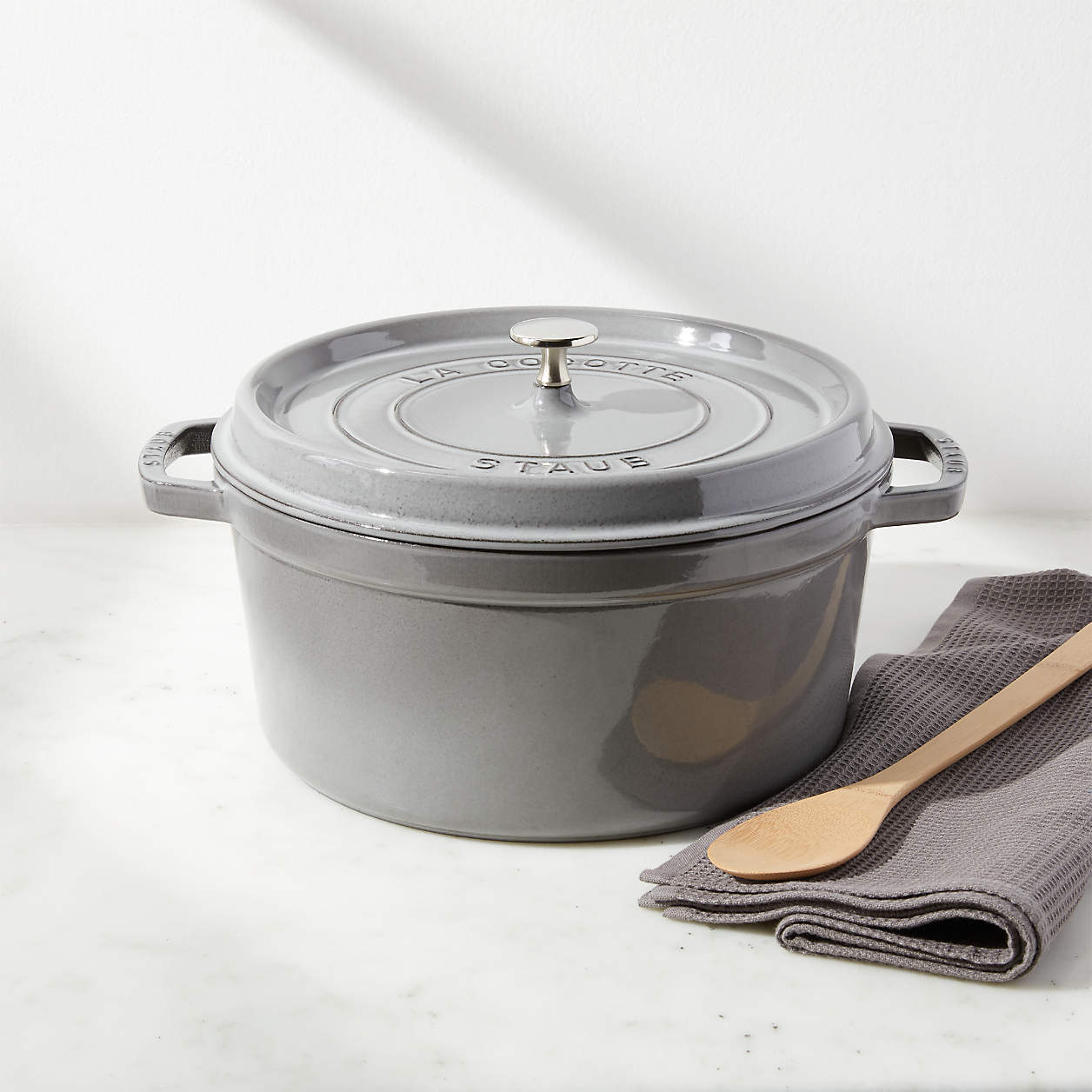 grey dutch oven on marble countertop with towel and wooden spoon.