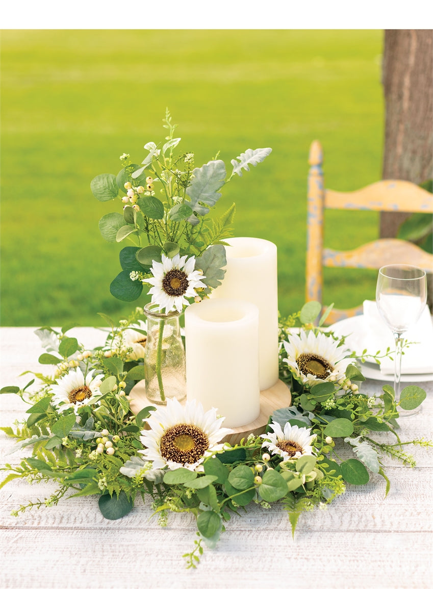 arrangement of artificial greenery on an outdoor table with candles, plates, and wine glass.