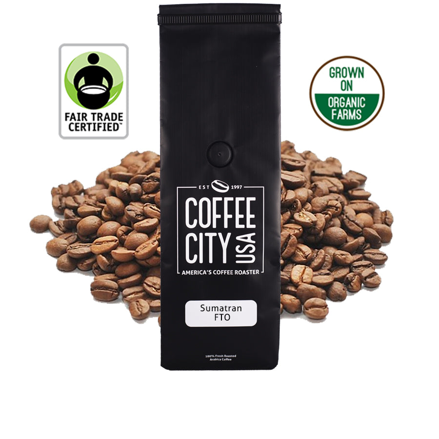 a black coffee bag filled with sumatra mandheling coffee with a pile of coffee beans behind it on a white background