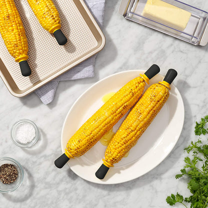 corn on cob on a platter and baking sheet drizzled with butter with corn holders in each end; stick of butter and dishes of salt and pepper on each side.