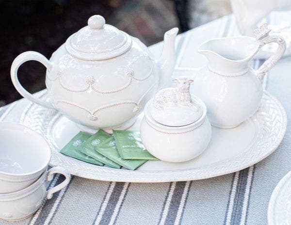 le panier large serving platter displayed with a teapot, creamer, sugar bowl and tea cups on a striped tablecloth