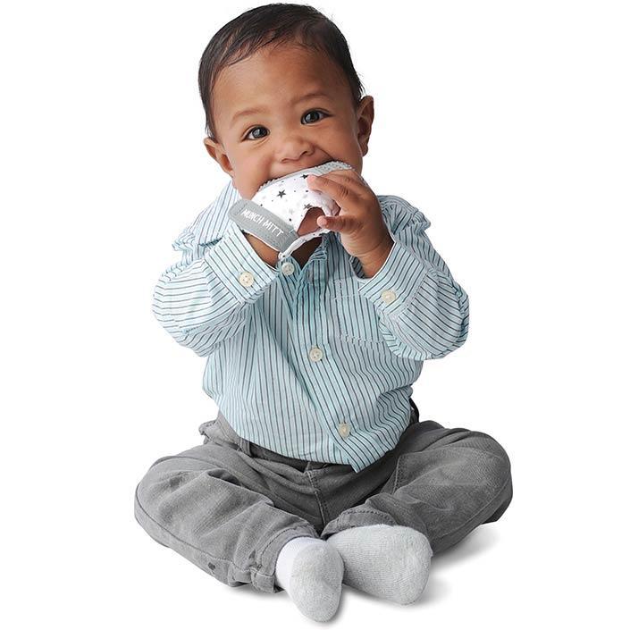a baby boy with the grey stars munch mitt on one hand and chewing on it against a white background