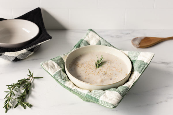 bowl of oats sitting inside the elm green bowl cozy displayed next to a sprig of tyme and wooden spoon and a white and gray marble surface 