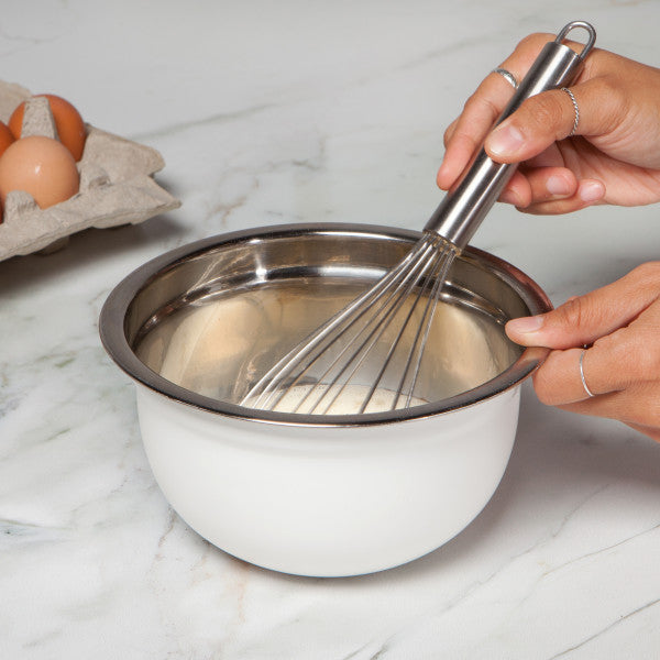 hands holding bowl and whisk stirring ingredients in bowl.