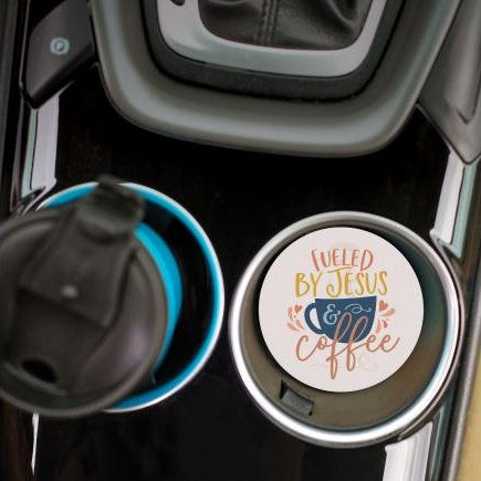 top view of the fueled by jesus and coffee car coaster displayed in the cup holder in a car