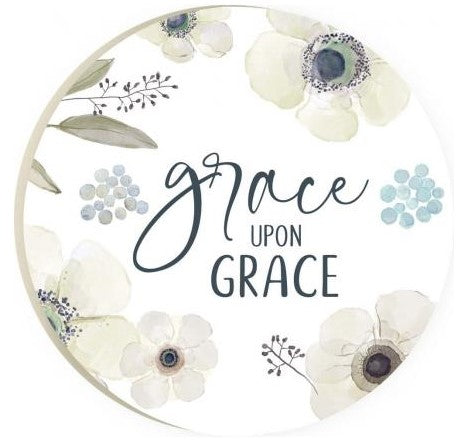 grace upon grace round coaster is white with blue and beige flowers, light green leaves and black text displayed on a white background